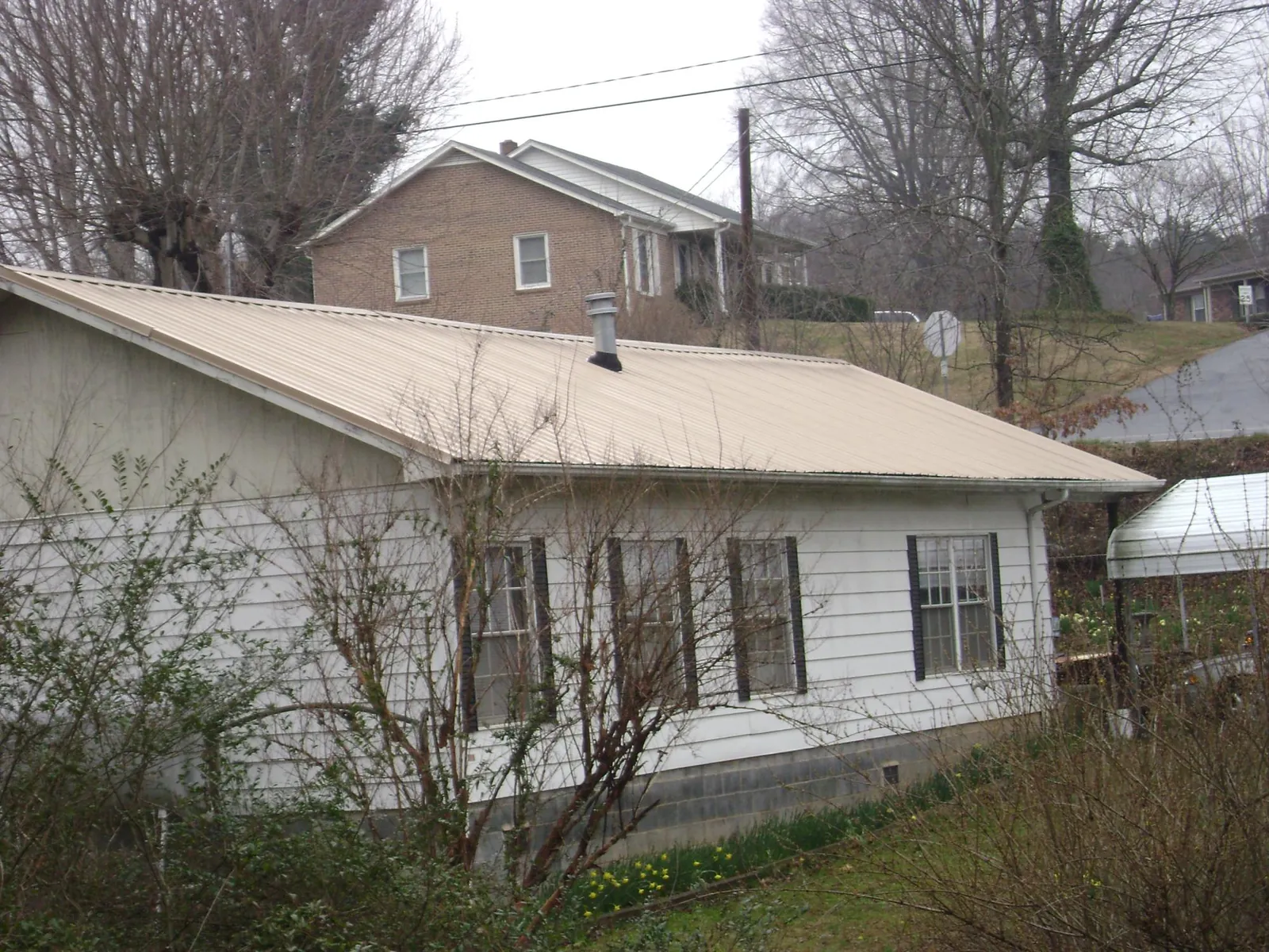 Tan metal roof on a white sided house set into a hillside — Commercial Roofing by Roofing Brothers in Coram